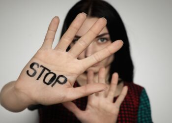 Young woman with word STOP written on her palm against light background, focus on hand