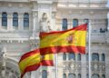 Primer plano de banderas de España ondeando al viento frente a un edificio emblemático de Madrid, simbolizando el impulso nacional al nuevo Plan de Derechos Culturales.