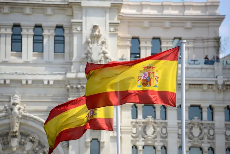 Primer plano de banderas de España ondeando al viento frente a un edificio emblemático de Madrid, simbolizando el impulso nacional al nuevo Plan de Derechos Culturales.