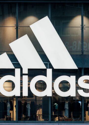 Vista frontal de una tienda Adidas con su logotipo iluminado, exhibiendo ropa deportiva en su interior.