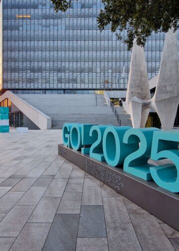 Escultura urbana con el logotipo “GO! 2025” en Gorizia, Italia, anunciando su designación como Capital Europea de la Cultura, con edificios modernos y atardecer de fondo.
