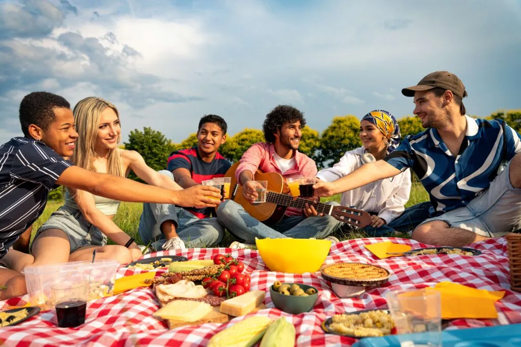 Grupo de jóvenes sentado sobre manta de picnic compartiendo bebidas y comida en un parque, representando el estilo de vida slow living y el equilibrio entre trabajo y bienestar.