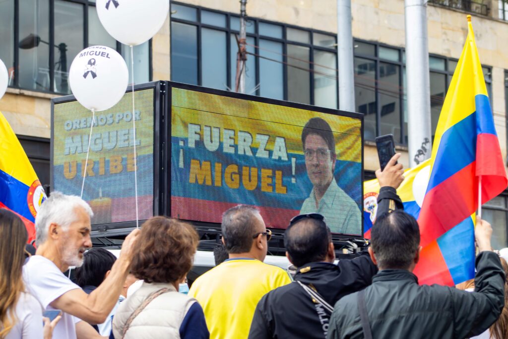 Grupo de personas sostiene globos y banderas de Colombia frente a una pantalla que muestra el mensaje “Fuerza Miguel” con la imagen de Miguel Uribe Turbay durante una concentración ciudadana.