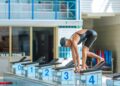 Deportista de natación adopta posición de salida en el bloque número cuatro durante una competencia en alberca cubierta.
