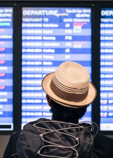 Persona con sombrero y mochila observa el tablero de información de vuelos de Aeroméxico en un aeropuerto.