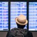 Persona con sombrero y mochila observa el tablero de información de vuelos de Aeroméxico en un aeropuerto.