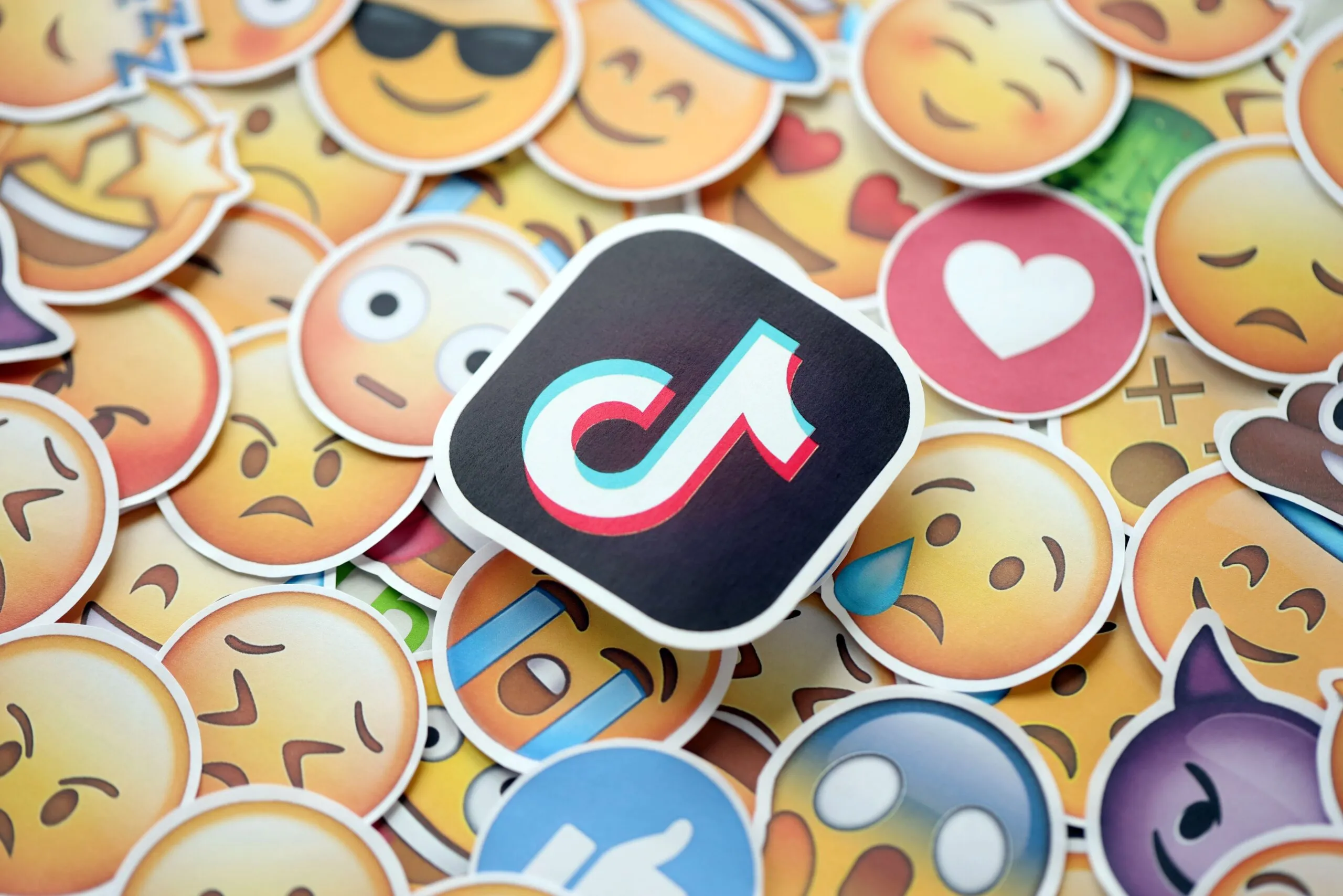 Sticker del logotipo de TikTok rodeado de emojis que simbolizan emociones digitales, ilustrando la controversia de Kendra Hilty sobre el uso de chatbots como herramienta de reflexión.