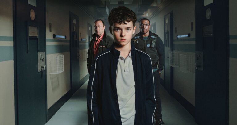 Protagonista juvenil de Adolescence en Netflix camina por un pasillo carcelario, acompañado por adultos, en una historia sobre masculinidad tóxica y educación.