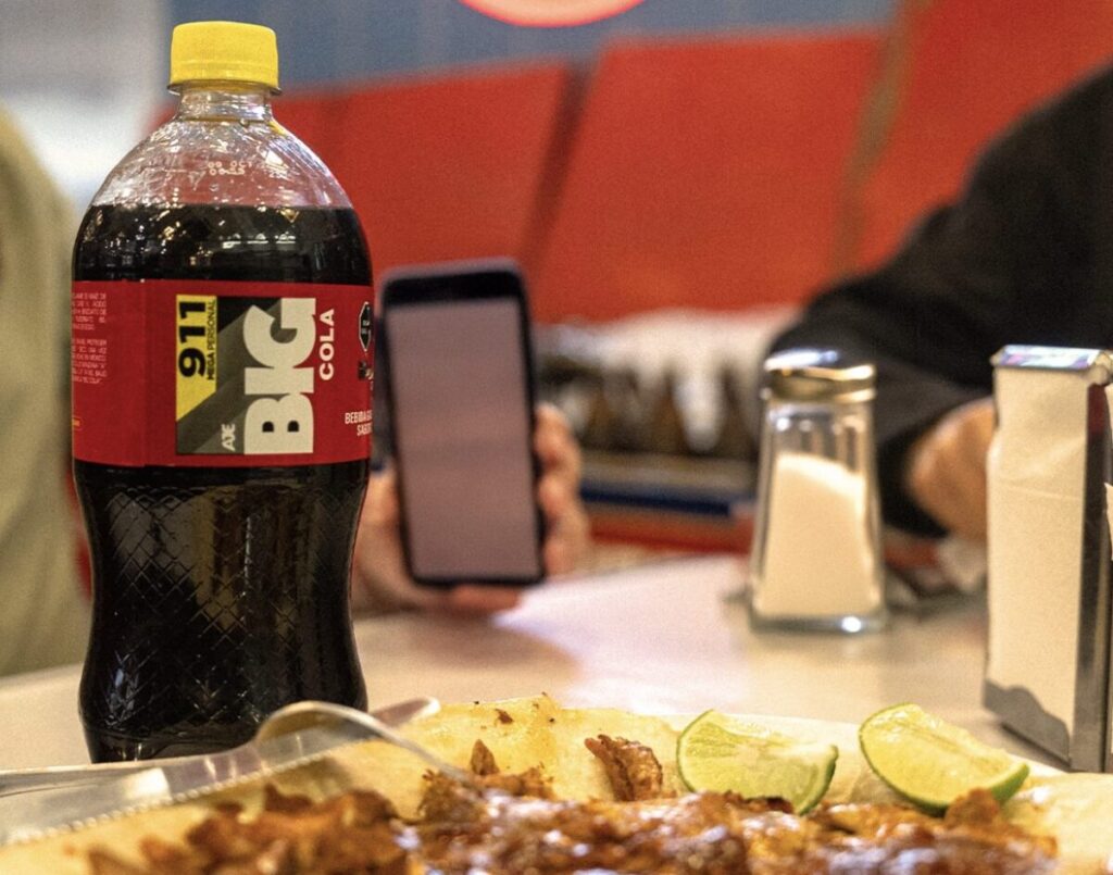 Botella de Big Cola servida junto a platillos típicos de la gastronomía mexicana.