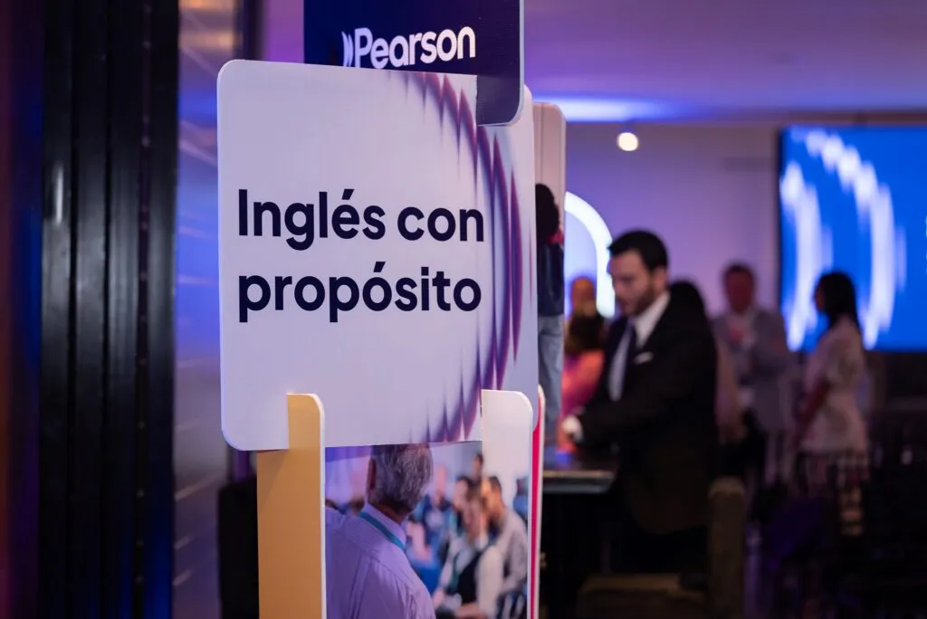 Señal con el texto “Inglés con propósito” en evento educativo de Pearson en Ciudad de México con asistentes al fondo