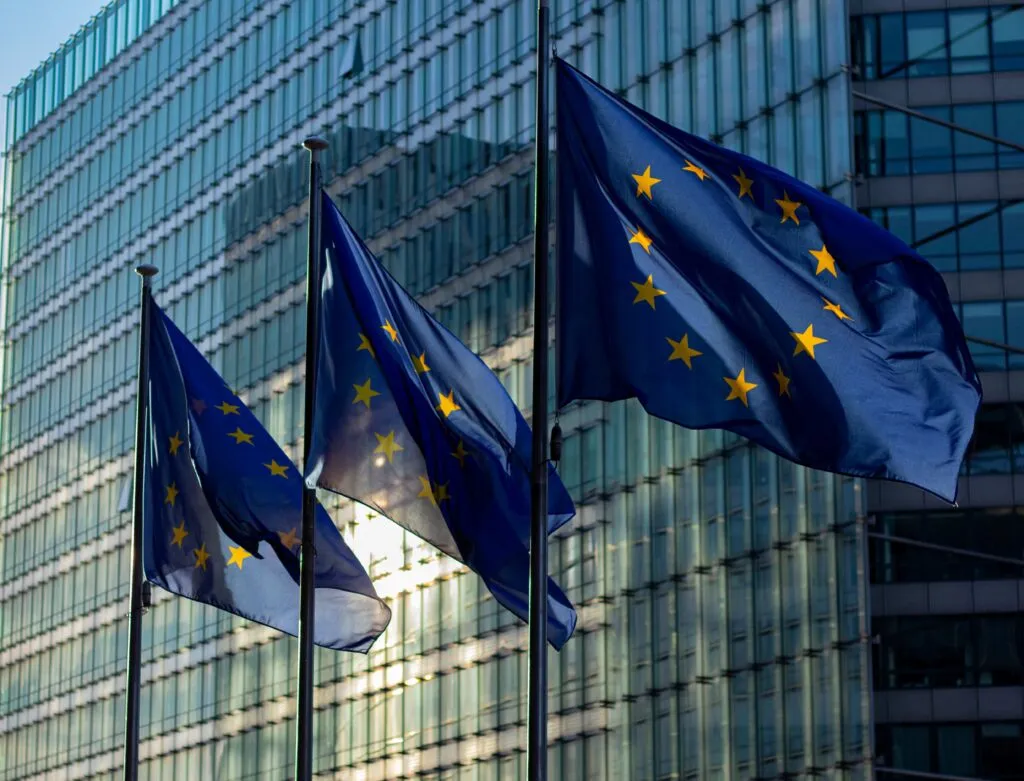 Banderas de la Unión Europea ondean frente a un edificio institucional, representando el compromiso europeo con la cultura, el patrimonio y la cooperación internacional.