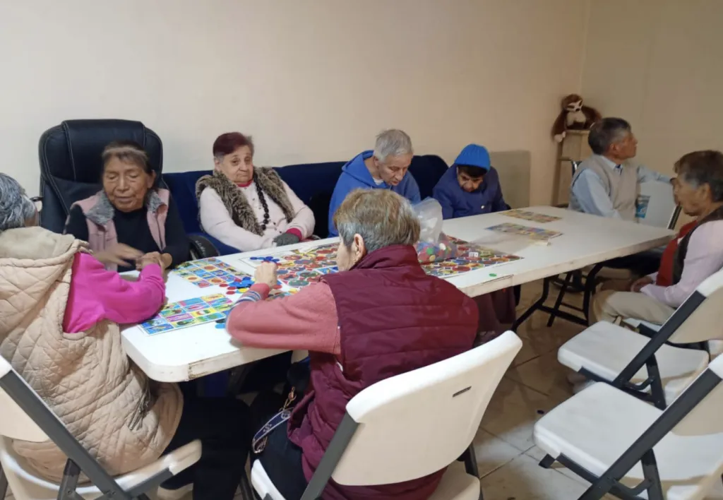 Personas adultas mayores conviven en un espacio comunitario mientras reciben apoyo nutricional y acompañamiento social de empresas como Corporativo Kosmos.